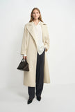 A model wearing an oatmeal oversized trench coat, open front, pairing charcoal wide-leg trousers.