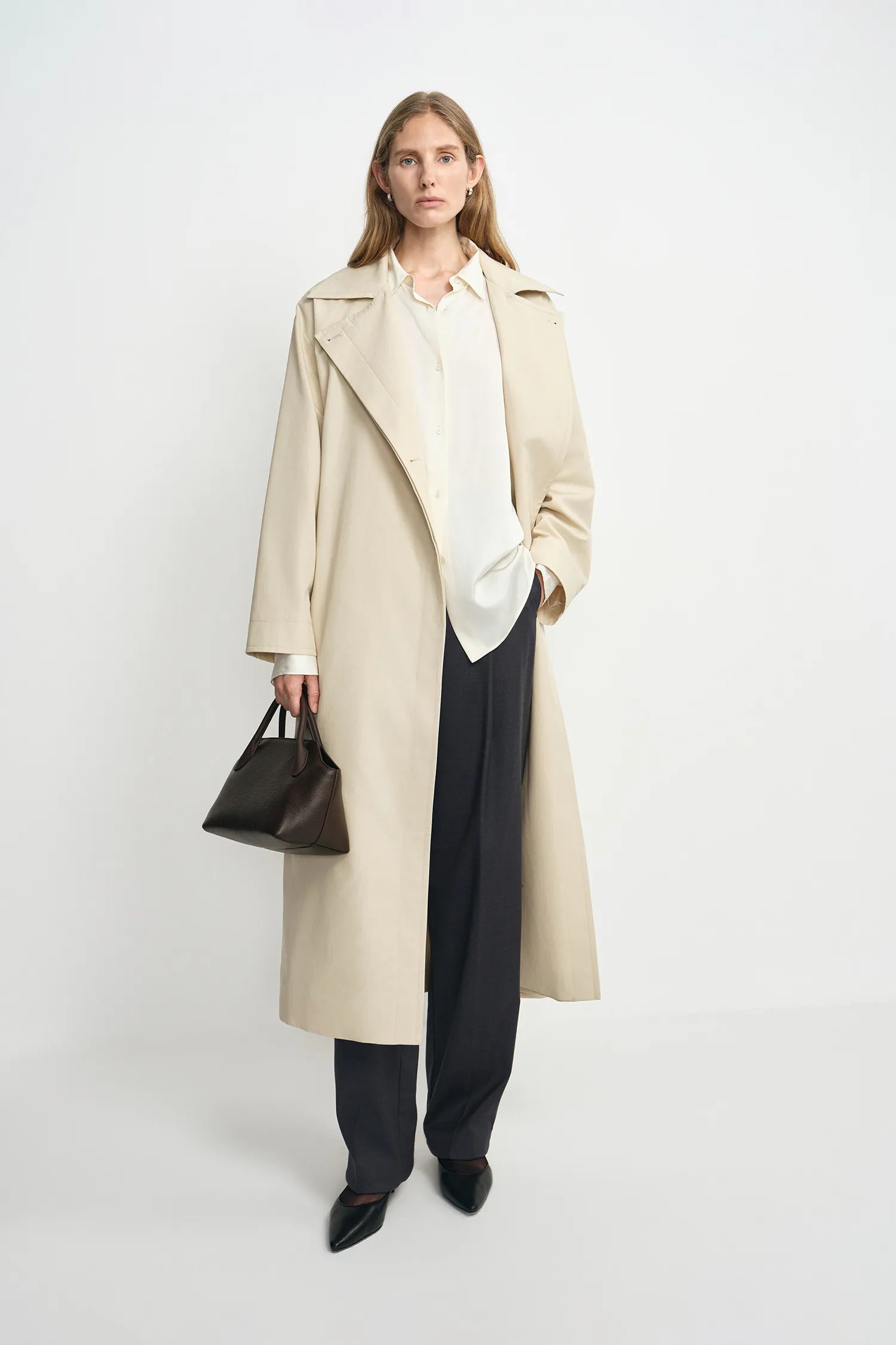 A model wearing an oatmeal oversized trench coat, open front, pairing charcoal wide-leg trousers.