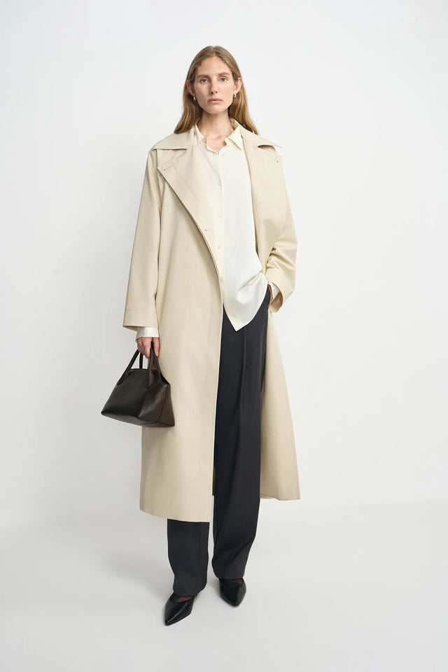A model wearing an oatmeal oversized trench coat, open front, pairing charcoal wide-leg trousers.