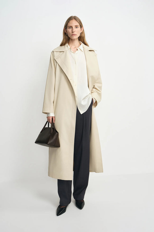 A model wearing an oatmeal oversized trench coat, open front, pairing charcoal wide-leg trousers.