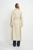 A model wearing an oatmeal oversized trench coat, pairing charcoal wide-leg trousers, back view.