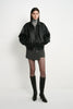 A model wearing a black faux leather bomber with oversized sleeves and a gathered hem, paired with a grey turtleneck, short grey skirt and black knee-high boots.