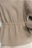 Close-up back view of a person wearing a taupe-beige long-sleeve knit top with an elasticated waist and light beige pants.