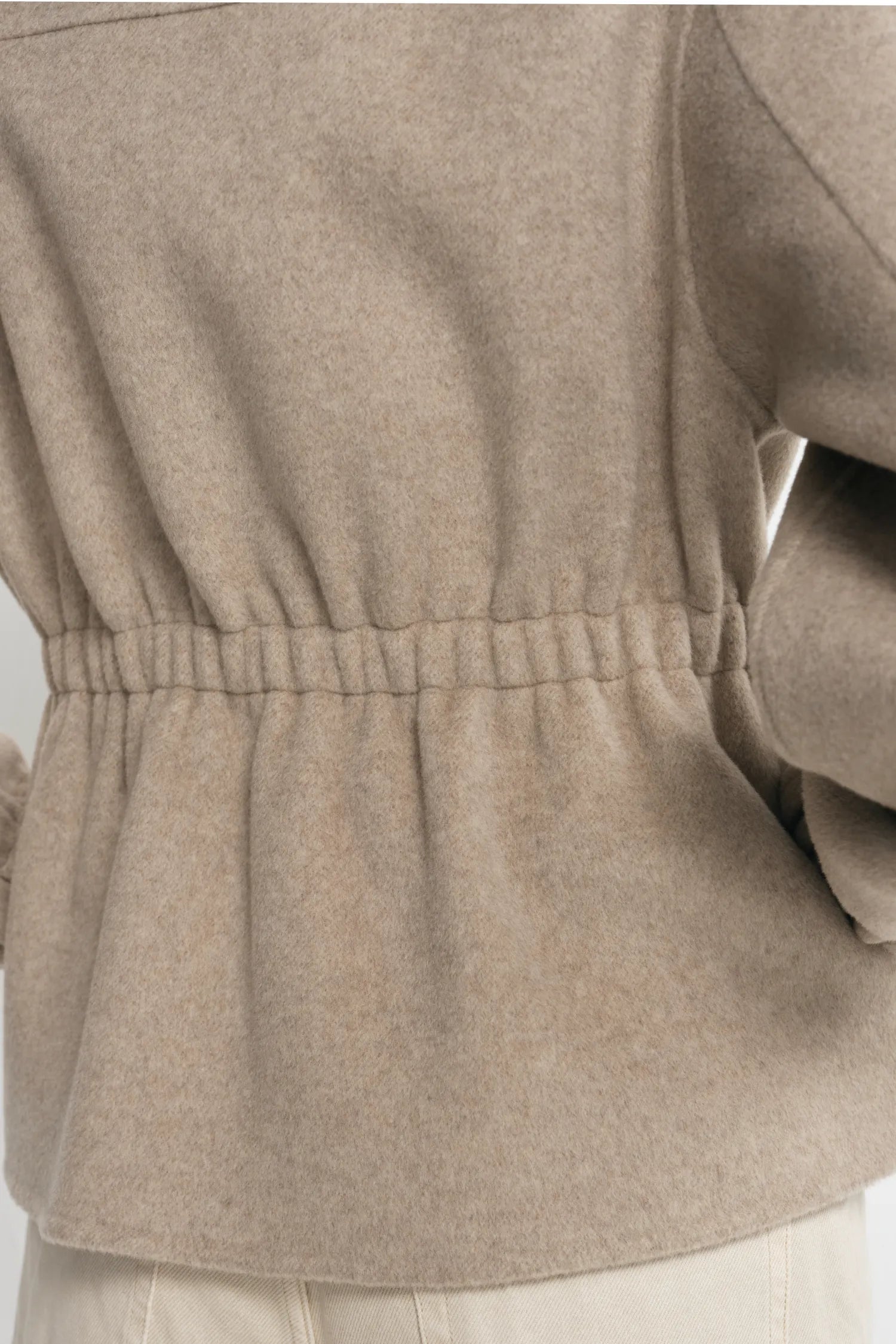 Close-up back view of a person wearing a taupe-beige long-sleeve knit top with an elasticated waist and light beige pants.