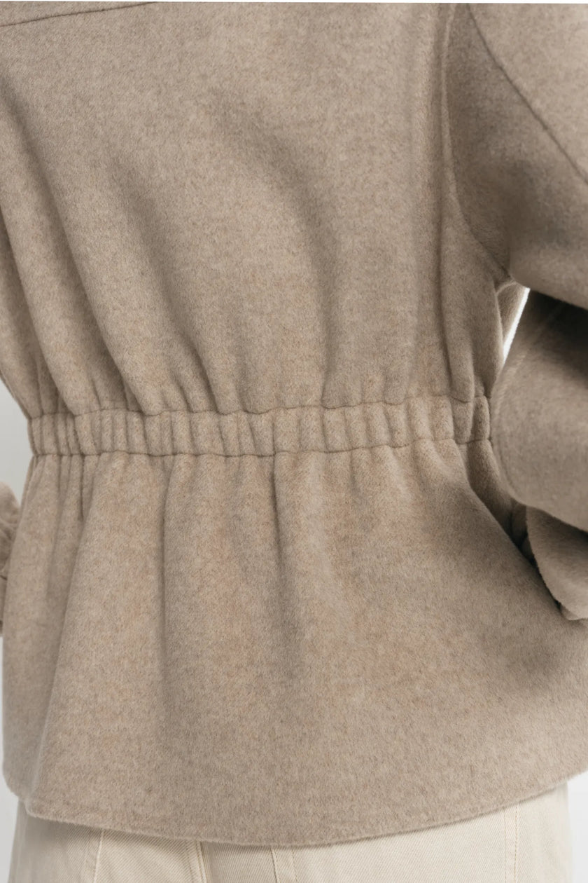 Close-up back view of a person wearing a taupe-beige long-sleeve knit top with an elasticated waist and light beige pants.