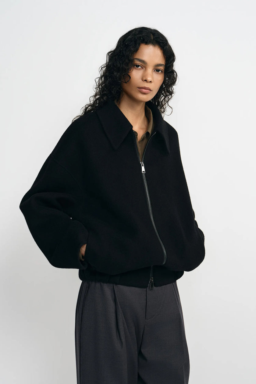 A model wearing a black zip-front jacket zipped up, showing the ribbed elastic hem at the waist.