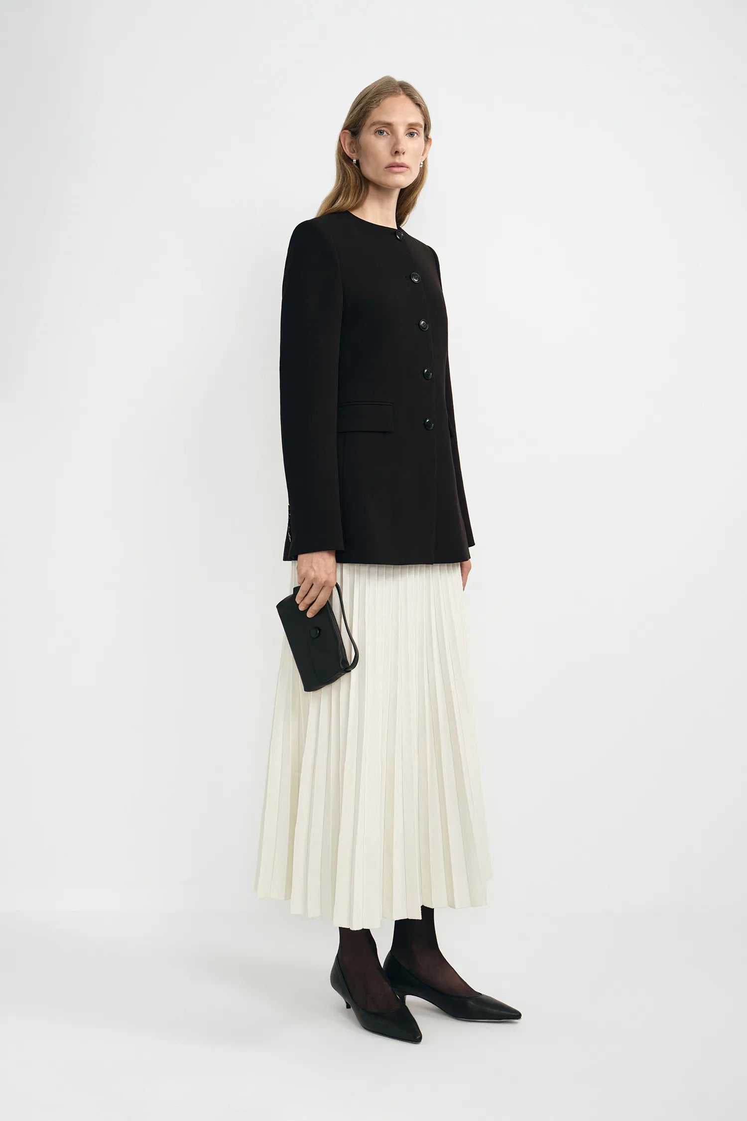 A model wearing a black collarless button-front jacket with front button closure and welt pockets.