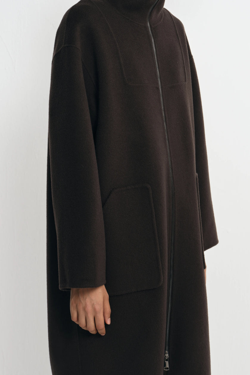A dark brown wool-blend coat with a high mock neck, front zipper, and large patch pockets, shown on a model against a light gray background.