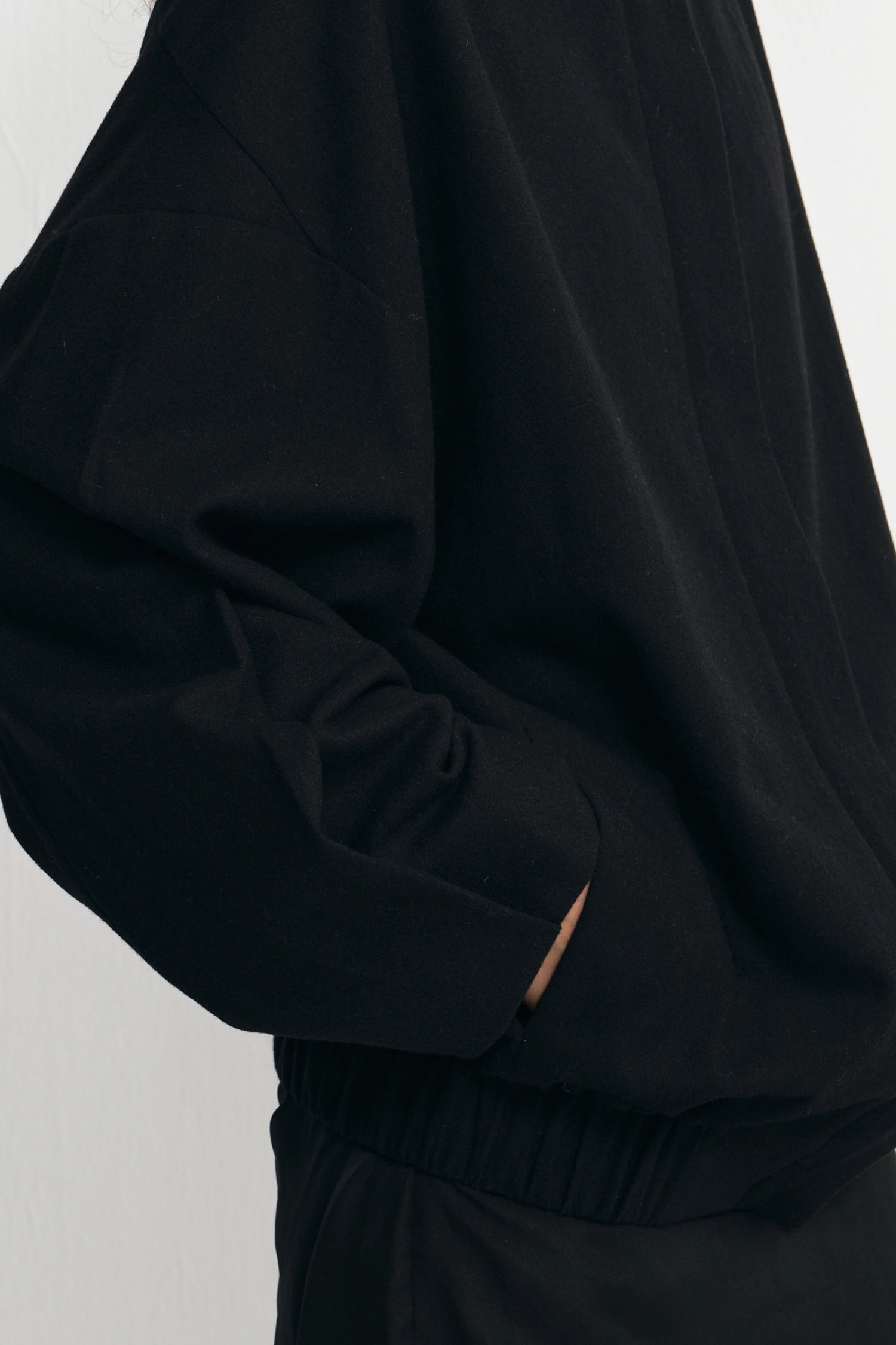 Close-up of a person wearing a black oversized long-sleeve top or jacket with a gathered elastic waist, shown against a plain light background.