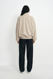 A person shown from the back wearing a light beige knit zip-up jacket and loose black wide-leg pants, standing against a plain white studio background.
