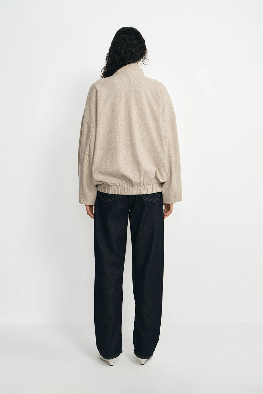 A person shown from the back wearing a light beige knit zip-up jacket and loose black wide-leg pants, standing against a plain white studio background.