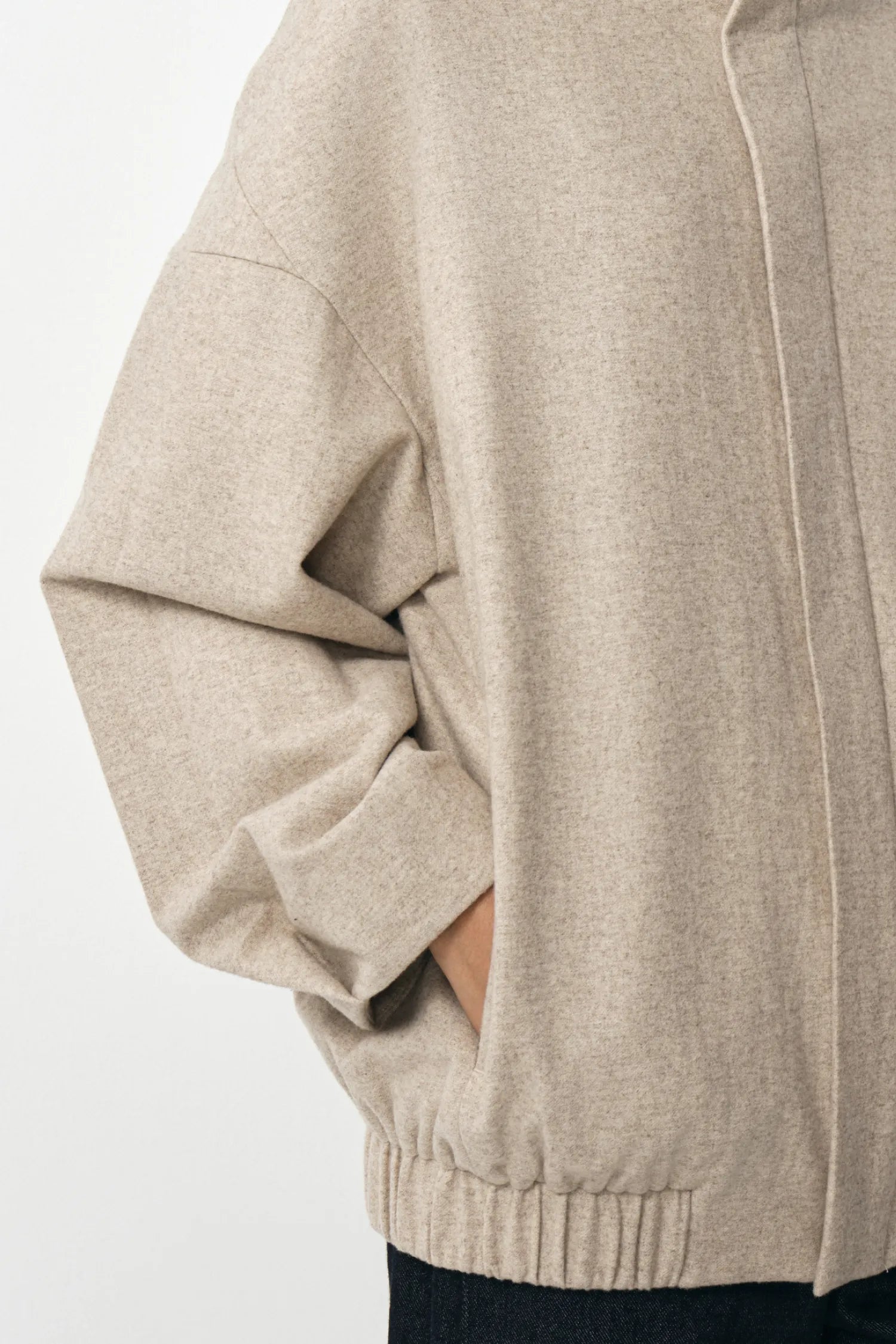 Close-up of a person wearing an oversized light beige knit sweater with long sleeves, ribbed cuffs, and a ribbed hem, shown against a plain light background.