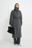 A model wearing a heather-grey wool-cashmere coat with the collar fastened high and waist belted, paired with charcoal trousers, white shoes and a black bag.