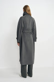 Rear three-quarter view of a model in a heather-grey belted coat, showing the raised collar and long straight hem above charcoal pinstriped trousers.