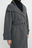 Close-up of a heather-grey wool-cashmere coat on a model, showing the wide collar with metal snaps, tied belt and folded cuffs over a black turtleneck.