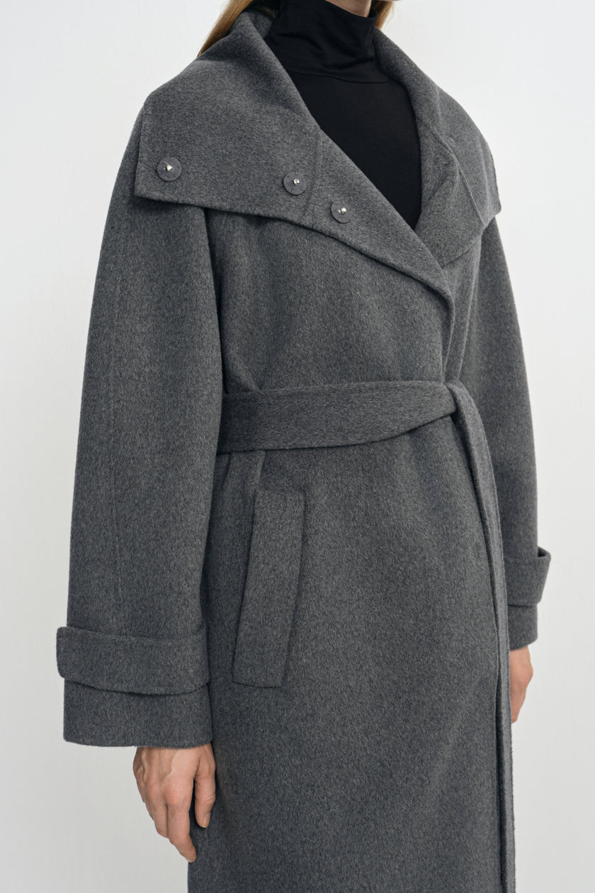 Close-up of a heather-grey wool-cashmere coat on a model, showing the wide collar with metal snaps, tied belt and folded cuffs over a black turtleneck.