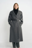 Front view of a model in a heather-grey coat with the collar folded wide and waist belted, hands in the pockets, worn over a black turtleneck.
