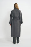 Back view of a model wearing a heather-grey wool-cashmere coat, with the belt drawing in the waist above a long hem and charcoal striped trousers.