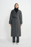 A model wearing a heather-grey wool-cashmere coat with a wide folded collar and tied waist, over a black turtleneck and striped trousers with white shoes.