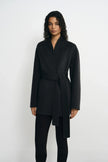 Front detail of a model wearing a heather-grey wrap coat, with the self-fabric belt tied at the waist and long ends falling over black leggings.
