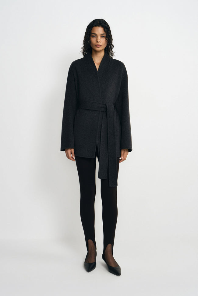 A model facing forward in a heather-grey wool-alpaca-blend short coat tied at the waist, styled with black split-hem leggings and pointed shoes.