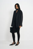 A model wearing a heather-grey wool-alpaca-blend short coat open with a dark neck scarf, paired with black leggings, pointed shoes and a black bag.