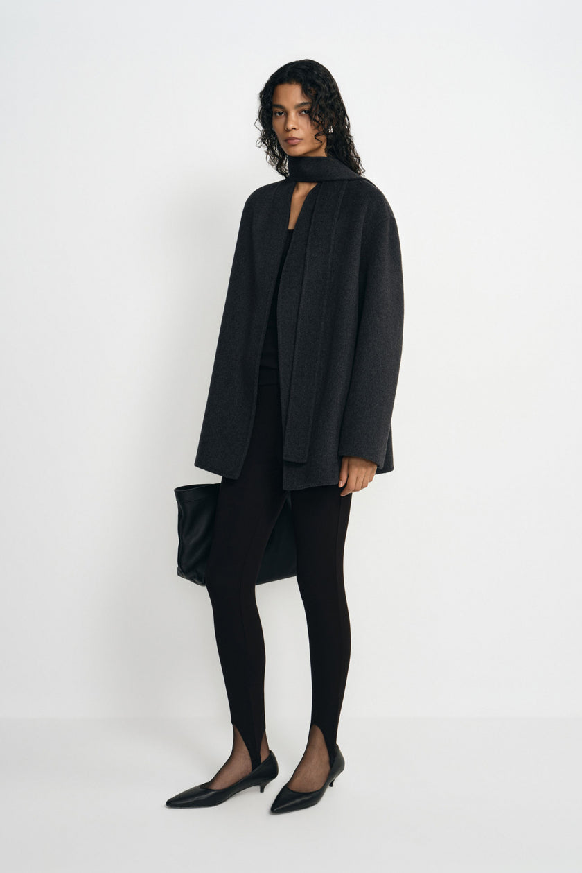 A model wearing a heather-grey wool-alpaca-blend short coat open with a dark neck scarf, paired with black leggings, pointed shoes and a black bag.