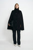 A model wearing a black wool-cashmere-blend cape coat with a pointed collar and button front, over a black turtleneck and dark trousers with white shoes.