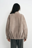 Back view of a slate-grey jacket on a model, showing dropped shoulders, a horizontal panel seam and a gathered hem above charcoal trousers.