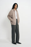 A model wearing a slate-grey calfskin jacket open over a white T-shirt and charcoal pinstriped trousers, with a gathered hem and black pointed shoes.