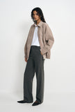 Three-quarter view of a model in an open slate-grey jacket with dropped shoulders, paired with a white T-shirt, charcoal striped trousers and black shoes.