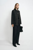 Angled view of a model in a grey plaid jacket with a contrasting black collar, styled with a black top, dark jeans, pointed shoes and a black handbag.