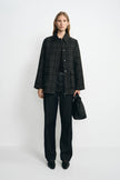A model facing forward in a grey plaid wool-blend jacket with a black sheepskin collar, paired with dark jeans, black pointed shoes and a black bag.