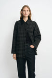 A model wearing a grey plaid wool-blend jacket with a contrasting black sheepskin collar, layered over a black top and dark jeans.