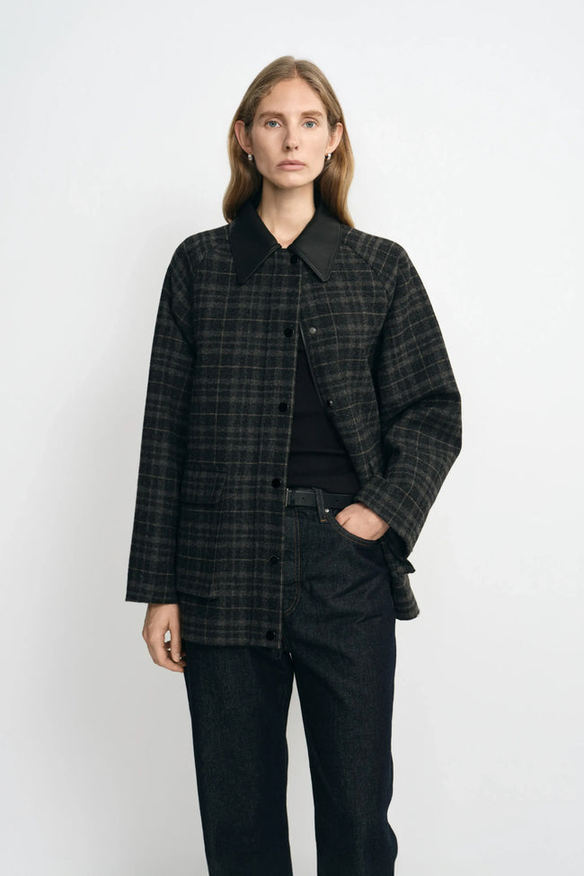 A model wearing a grey plaid wool-blend jacket with a contrasting black sheepskin collar, layered over a black top and dark jeans.