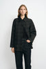 A model wearing a grey plaid wool-blend jacket with a contrasting black sheepskin collar, layered over a black top and dark jeans.