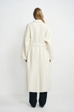 Back view of a model wearing a winter-white wool coat, with the belt gathering the waist above a long hem and dark jeans.