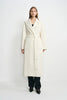 A model wearing a winter-white 100% wool wrap coat with notched lapels and a tied waist, paired with a black top, dark jeans and pointed black shoes.