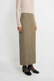 A model wearing an oatmeal pencil midi skirt, side angle detail showing the fitted waist and straight silhouette, pairing black sheer tights and Mary Jane heels.