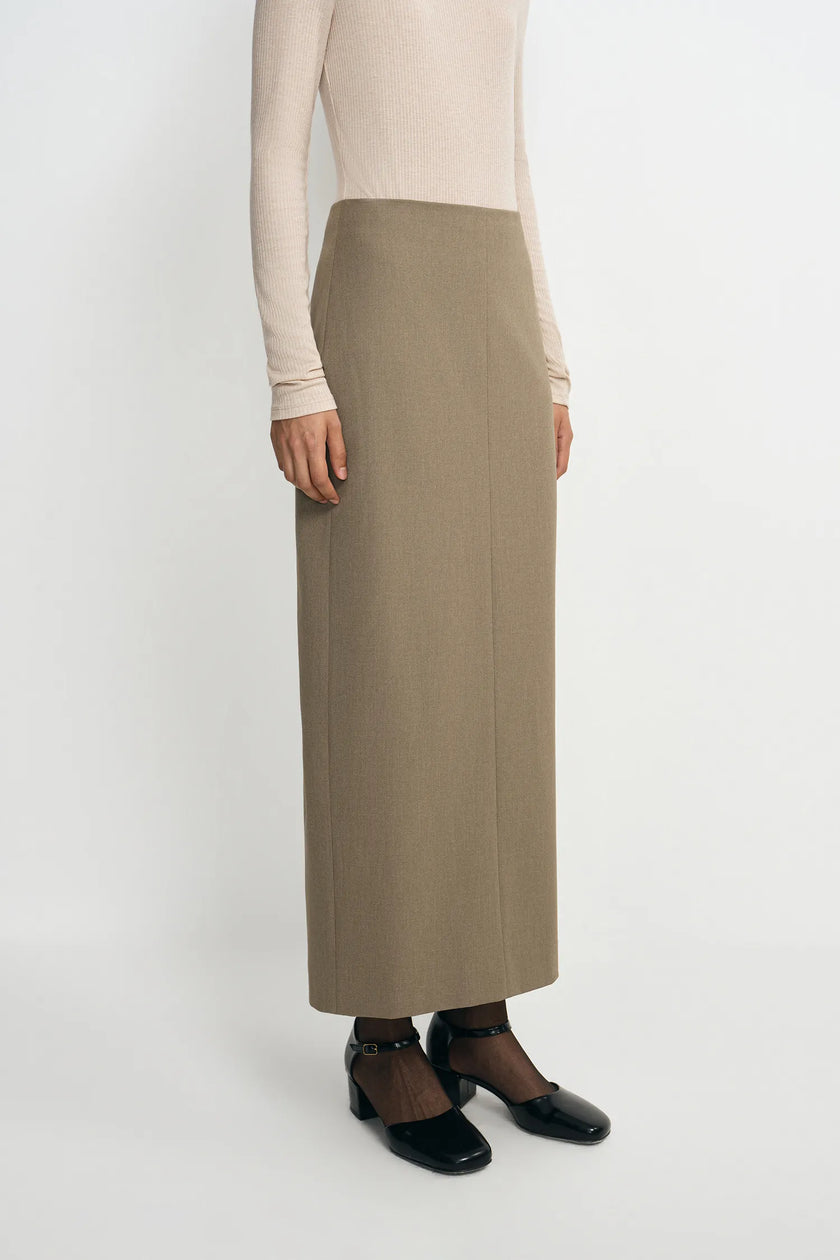 A model wearing an oatmeal pencil midi skirt, side angle detail showing the fitted waist and straight silhouette, pairing black sheer tights and Mary Jane heels.