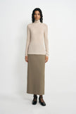 A model wearing an oatmeal pencil midi skirt with a slim tailored fit, pairing a beige turtleneck top and black Mary Jane heels.
