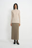 A model wearing an oatmeal pencil midi skirt with a slim tailored fit, pairing a beige turtleneck top and black Mary Jane heels.
