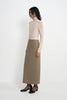 A model wearing an oatmeal pencil midi skirt, side view showing the clean vertical seaming and fitted silhouette, pairing a beige turtleneck top and black Mary Jane heels.
