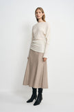 Three-quarter view of a model in an oatmeal wool midi skirt, with the flared hem below an untucked cream top and above black boots.
