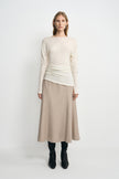 A model facing forward in an oatmeal wool midi skirt with an A-line silhouette, styled with a cream long-sleeve top and black boots.
