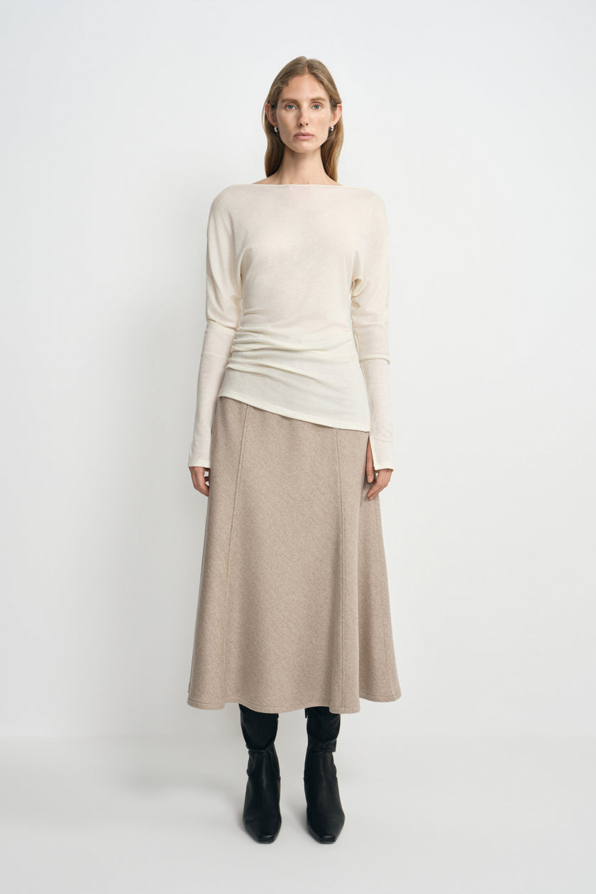 A model facing forward in an oatmeal wool midi skirt with an A-line silhouette, styled with a cream long-sleeve top and black boots.