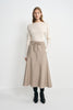 A model wearing an oatmeal 100% wool midi skirt with long waist ties and a flared hem, paired with a tucked cream top and black heeled boots.