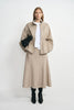 A model wearing an oatmeal 100% wool midi skirt with a flared hem, paired with a beige jacket, white T-shirt and black heeled boots.