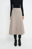 A model wearing a black long-sleeve top and a high-waisted, A-line midi skirt in a textured light beige or taupe knit. The model is also wearing black knee-high boots, photographed against a seamless white studio background.