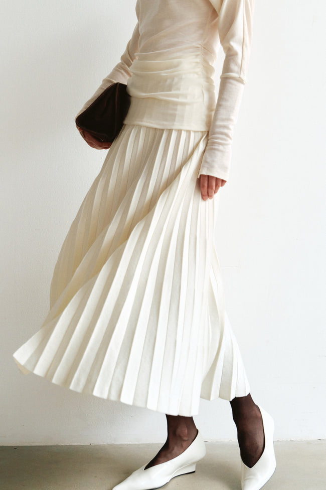 Close-up of the Amélie Accordion-Pleat Skirt in ecru, showing narrow accordion pleats in motion with a cream ruched top and white pointed shoes.